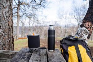 Mountaineering equipment for hiking in the mountains, yellow backpack, a set of equipment in the forest, hiking, a picnic in nature, dishes in a campsite, a thermos with a mug. photo