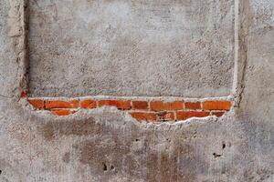 Minimalistic frame of the wall. Through a thick layer of cement, brickwork is visible. Solid red brick wall. Urban interior photo