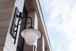 A street lamp hangs on the wall of the house. Evening lighting, a lamp against the sky. Architecture of the building. photo