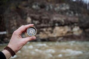 A man's hand holds a compass against a rock, orienteering in the wild on a compass, an arrow pointing north. photo