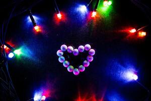 The heart is lined with white candy. Figurines of sweets. Abstract photos against a background of bright lights. Festive mood, glare from the garland