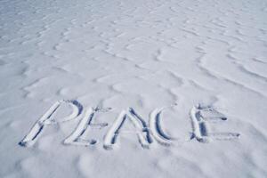 Peace is written in the snow, the concept of no war is indicated by letters on a white background, a snow inscription in winter, an art symbol of peace. photo