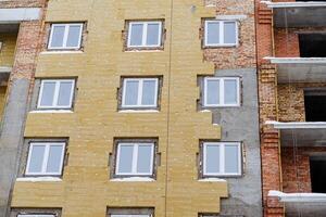 un cerca Disparo de el ventanas de un recién construido casa. fachada revestimiento con aislamiento material. construcción de un nuevo residencial edificio para gente. foto