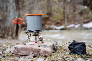 Camping equipment for cooking in nature, gas burner against the background of the river, a pot of food on the fire, dishes on a hike, camp by the water lunch photo