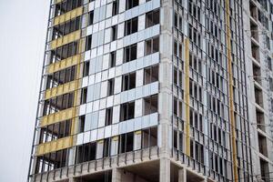 The facade of the house outside is insulated with mineral wool. Put glass in the windows of a high-rise building. Construction of apartments, facing the house with aluminum profile. photo