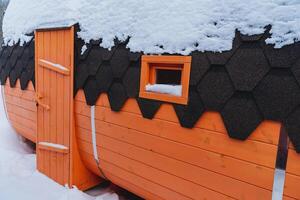 View on the side of a wooden bath, painted orange, protective paint against mold and aging of the tree. The bath barrel stands outside in winter. Wooden door, window in the wall. photo