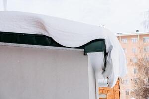 ventisquero cuelga desde el bloque de techo de nieve en el fachada de el edificio.calle limpieza en invierno. ciudad edificios debajo el nieve. de invierno ven foto