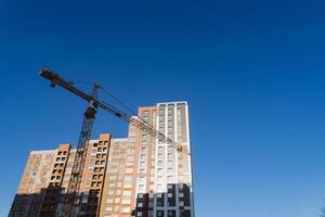 A crane builds a house at a height, lifts the load to the upper floor. The construction site of a residential building, a building against the sky. photo