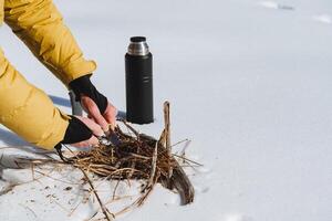 A man lights a fire in the snow. Survival in harsh extreme winter conditions. The thermos stands on the snow, hands carving out sparks of silicon. photo