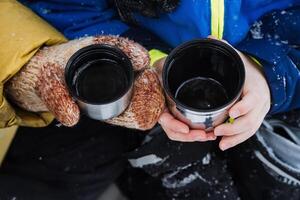 Thermo mug in hand. A hand holds a mug of hot tea. Drink tea in the winter outside. A metal cup with a drink is held by a person. Tea from a thermos. photo