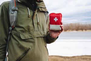 A red first aid kit bag is held in the hand of a person, camping equipment for a hike, survival in the forest is the first emergency help for injury. photo