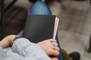 A notepad for the record lies on the girl's lap. Black notebook diary. A person sits in an auditorium at a lecture. photo