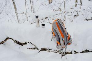 Thermos with a mug, a backpack lies on the snow. Stop on the road for lunch. Stop on the route to drink hot tea. Hiking equipment. photo