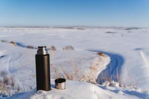 Equipment, equipment for a hiking trip, a thermos in the snow, a vacuum bottle for hot drinks. Nature of Russia. photo