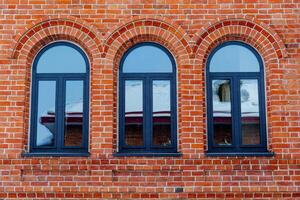 Minimalistic shot of a brick wall with windows. Three arched windows with plastic frame. Red brick masonry. Building a house or wall. Repeating pattern photo