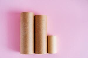 Three elongated tubes of craft paper. Cardboard packaging. Tubes for storing pencils and pens on a pink background. Packing set photo