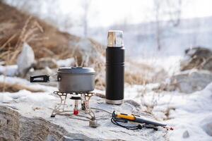 Camping equipment set for survival in the forest, mountain hike, dishes for cooking in the camp, black thermos with tea, pot pot standing on a gas burner, knife photo