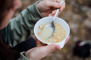 allí es sopa con un cuchara, un plato de comida Disparo de cerca, el concepto de turista comida en un caminata, un instante almuerzo, picatostes flotante en el sopa. foto