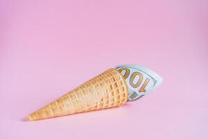 A hundred dollars in an ice cream cone. Unusual ice cream with a bill. A horn with money on a pink background. Interesting and abstract subject shooting photo