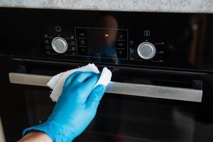 Wipe the gas stove with a rag. Cleaning the house. A blue glove holds a white rag. Wash the metal door handle. photo