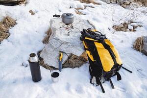 Hiking equipment, food backpack, gas burner, fire cooking pot, thermos with tea, snow camp in the mountains, winter hike, trekking photo