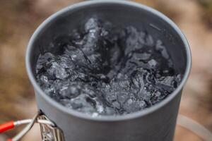 Boiling water in a pot, Shot close-up of water bubbles when heated, tourist pot, brewing tea, cooking on a hike. photo