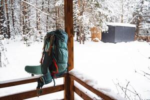 A bright hiking backpack lies on the snow. A climbing rope is tied to a backpack. In the side pocket of the thermos. Hiking in winter. Rocks and forests photo