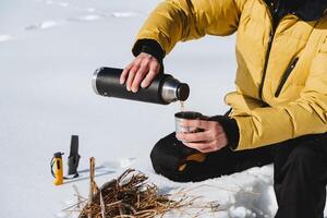 Hands pour hot tea from a thermos into a mug. Camping in nature, winter hiking in the cold season. A person drinks a hot drink from a cup. photo