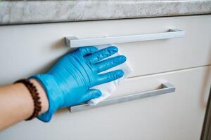 Wet cleaning, wipe the dust off the surface of the cabinet. Wash the box with cleaning agent. A hand in a blue glove against the background of a white box. Housekeeping. photo