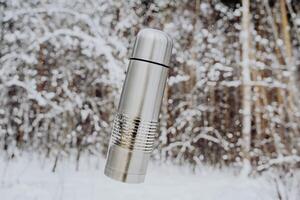 The thermos flies in the air. Vacuum bottle concept. Winter landscape. Metal flask for hot tea. photo