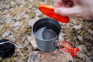 An aluminum pot stands on a gas burner, open the lid of the pan to see the boiling water, a pan with handles, tourist utensils for cooking on a hike. photo