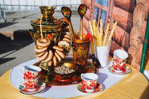 platos pintado con khokhloma estar en el mesa, un Samovar elaborada con té, tilo pétalos mentira en un bol, Bagels colgar en un cuerda. foto