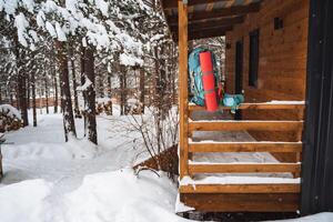 A bright hiking backpack lies on the snow. A climbing rope is tied to a backpack. In the side pocket of the thermos. Hiking in winter. Rocks and forests photo