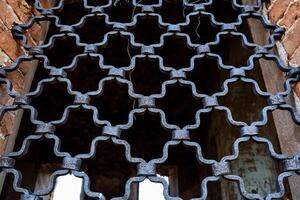 Forged lattice on the window of an old building, beautiful pattern of binding of metal rods, decoration of an ancient temple, repetitive ornament of old iron, passage photo