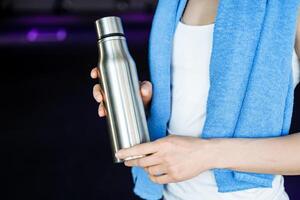 A bottle of water against the background of the girl's athletic body. Drinking regimen during exercise. A blue towel hangs around my neck. Thermos with hot tea. energy drink. photo