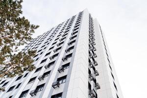 An apartment building rising high up to the sky. Trees near the residential complex. Facade of an apartment building. perspective, smooth lines of the building photo