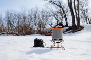 The concept of tourist utensils stands on the snow against the background of the forest, hiking equipment, breakfast in nature in the spring, boil water in a pot in nature, sunny weather photo