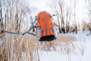 The orange-colored backpack hung in the air. The concept of camping equipment. The flight of a backpack against the background of the forest. Sports equipment for climbers. photo