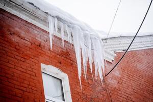 Ice icicles hang on the roof, the danger of ice falling on the head. A place of increased danger to life. The threat of snow falling from the roof. photo