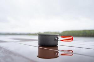 A plate made of aluminum stands on the table, tourist dishes, food on a hike, rain puddle on the table, reflection of a cup in the water, cloudy weather on a hike in the mountains photo