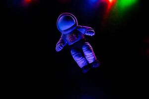 minimalista Disparo de juguetes, un juguete astronauta mentiras en un oscuro antecedentes. espacio vuelos, juguetes para niños hecho de el plastico y polímero arcilla. destello desde el guirnalda foto