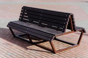 A wooden bench stands outside, a place to sit, rest in the park, a double bench stands on the sidewalk. photo