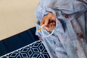 A Muslim woman wearing a moslem clothes with hijab called mukena and holding prayer beads for praying or dhikr photo