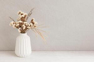 Minimalistic composition of dried flowers in white vase on gray vintage textured wall background and on wooden shelf. Front view, mock up, copy space photo