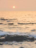 Sea sunrise with rock on beach photo