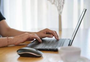 Close up of woman hands working with laptop while sitting at desk with a cup of coffee at home photo