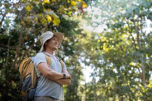 Young man asian trekking among trees with backpack, young man enjoy alone in forest. Camping, hiking, travelling, search for adventure concept photo