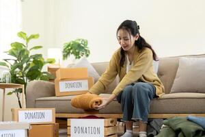 Woman asian holding donation box full with clothes and select clothes. Concept of donation and clothes recycling. Helping poor people photo