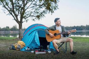 hombre asiático de viaje con tienda cámping en montaña parte superior al aire libre aventuras estilo de vida excursionismo activo verano vacaciones mientras jugando guitarra foto