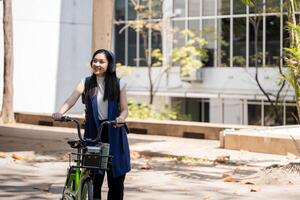 Eco friendly, Happy lifestyle asian beautiful young businesswoman riding bicycle go to office work at city street with bicycle in morning photo